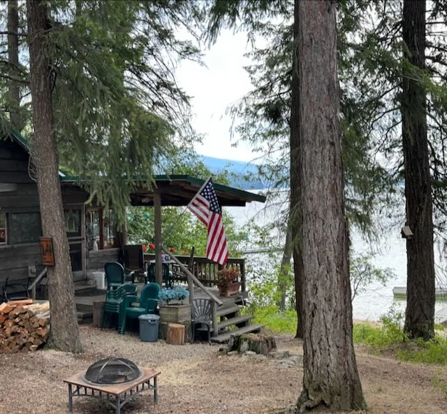 Cabin among tall trees with the lake visible beyond the covered deck