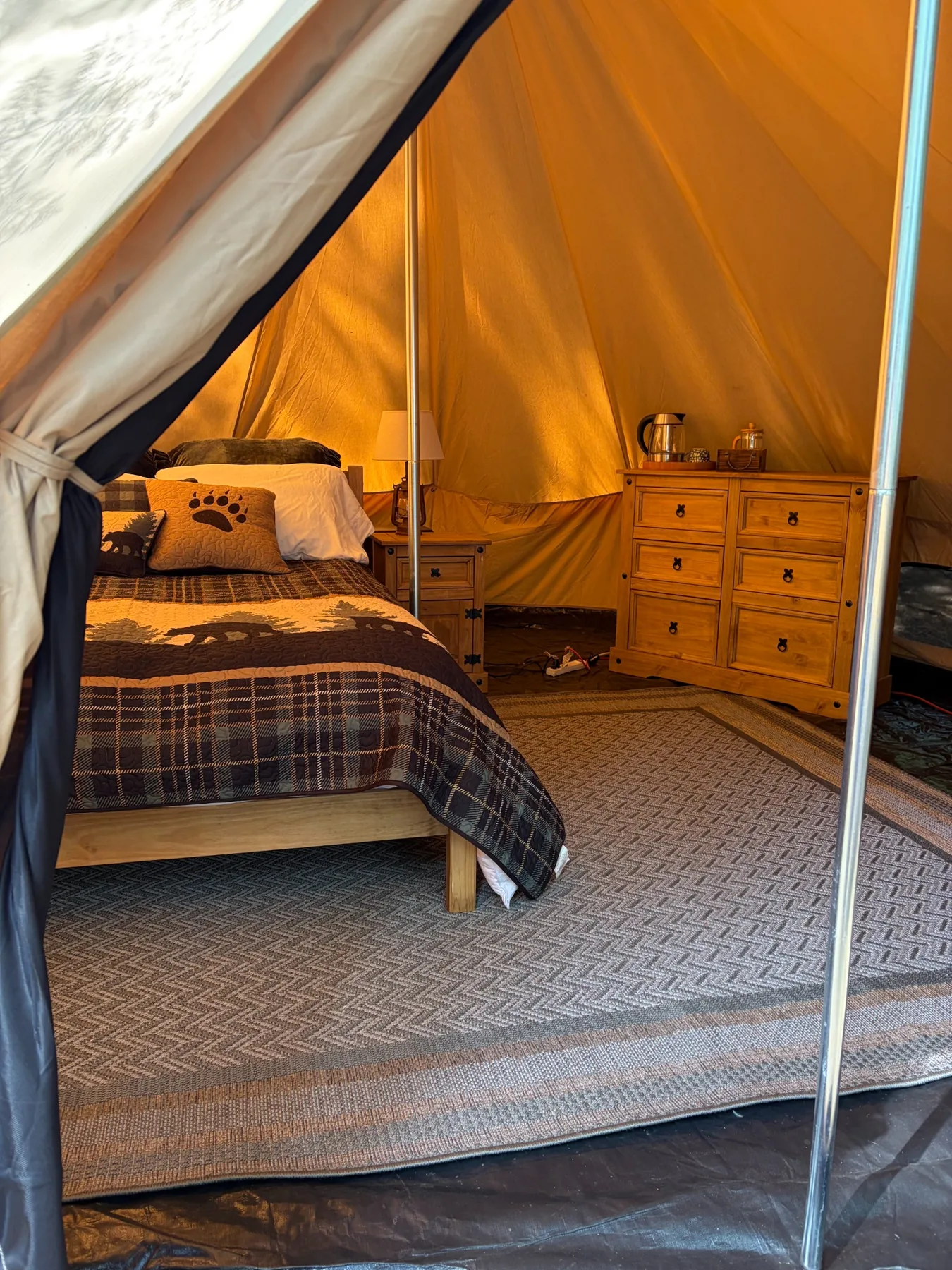 Tent interior showing queen bed, dresser, rugs and coffee kettle