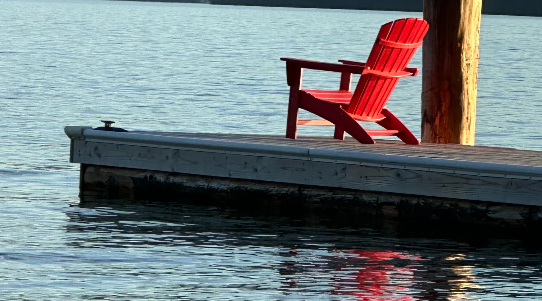 Red Adirondack chair on the dock overlooking Priest Lake and surrounding mountains